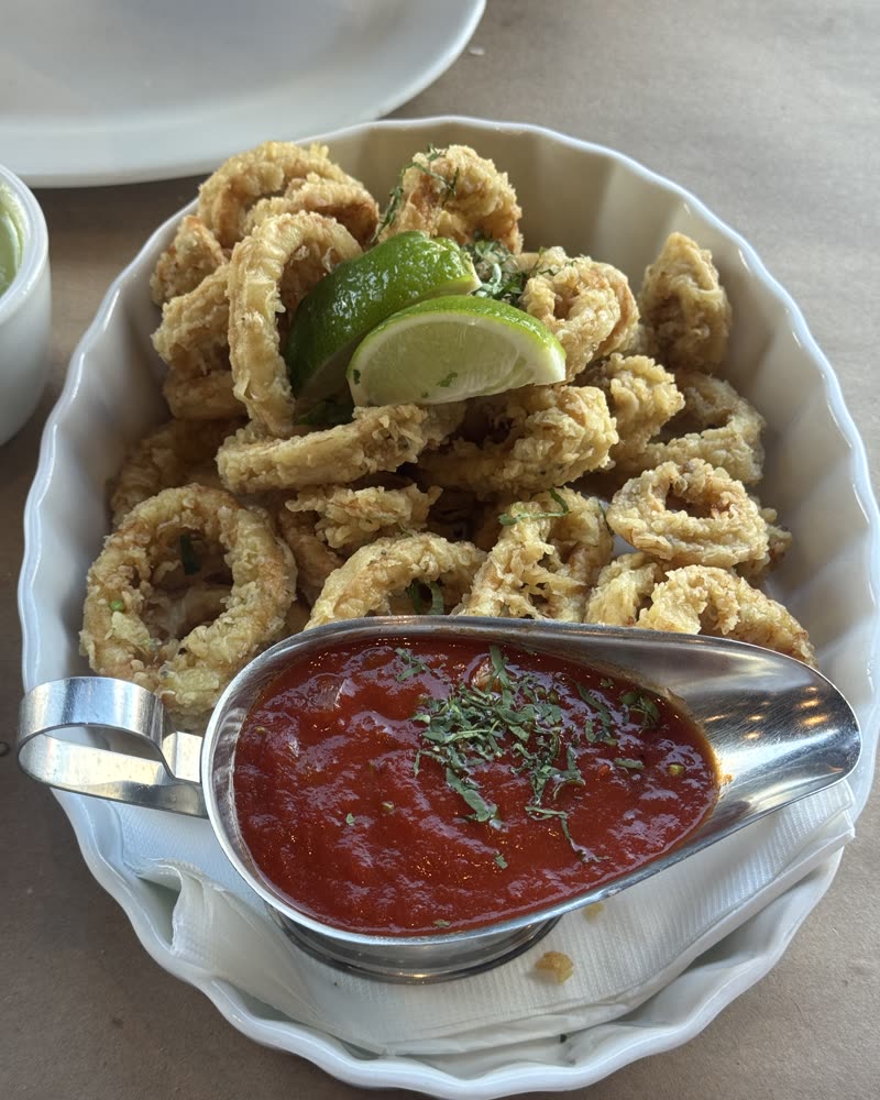 A plate of fried calamari with lime wedges and marinara sauce